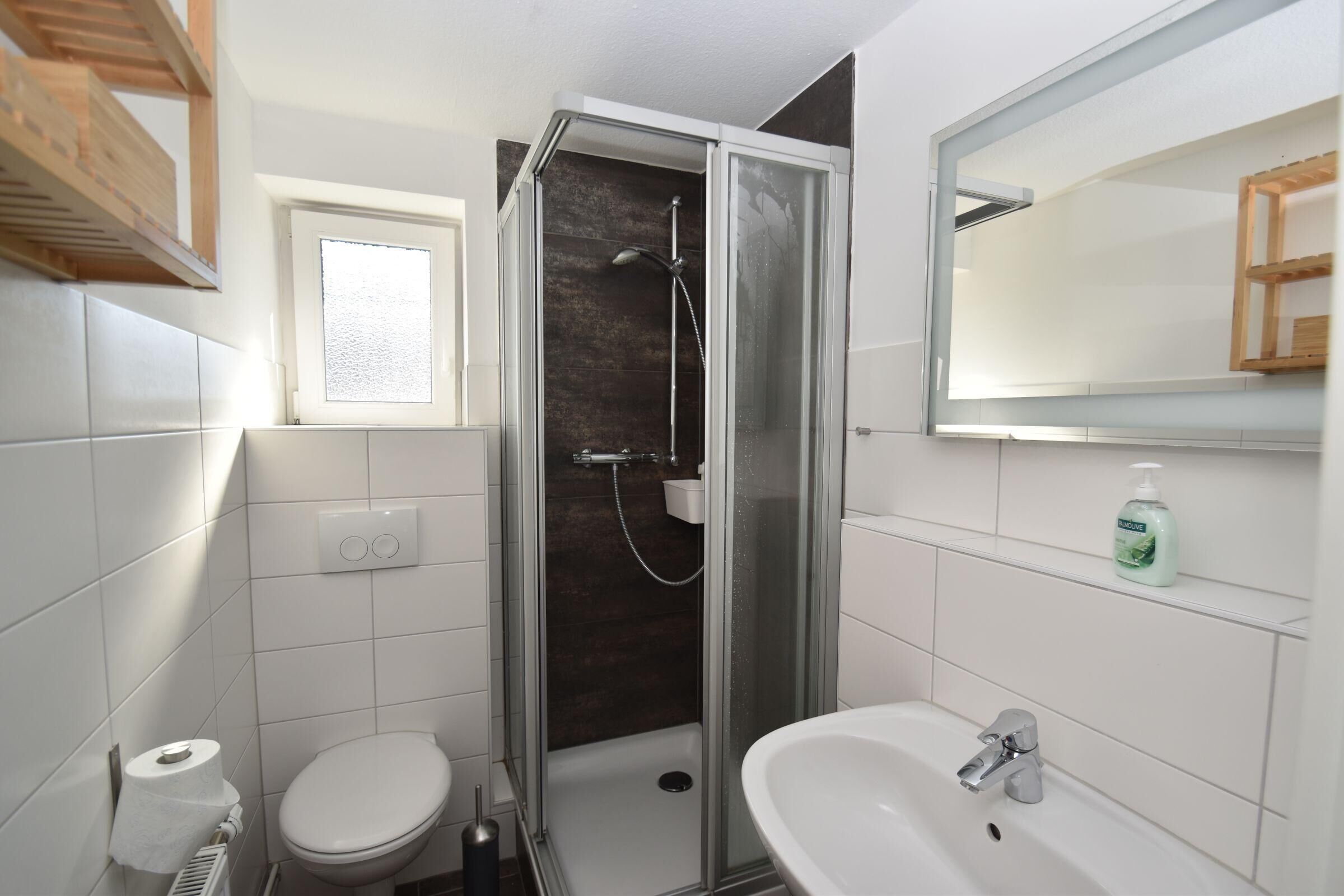 A bathroom with a glass-enclosed shower, a toilet, a sink, and a window.