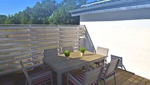 A wooden deck with a table and chairs, potted plants, and a white fence.