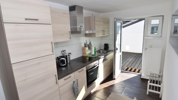 A modern kitchen with light wood cabinets, stainless steel appliances, and a view to the outside.