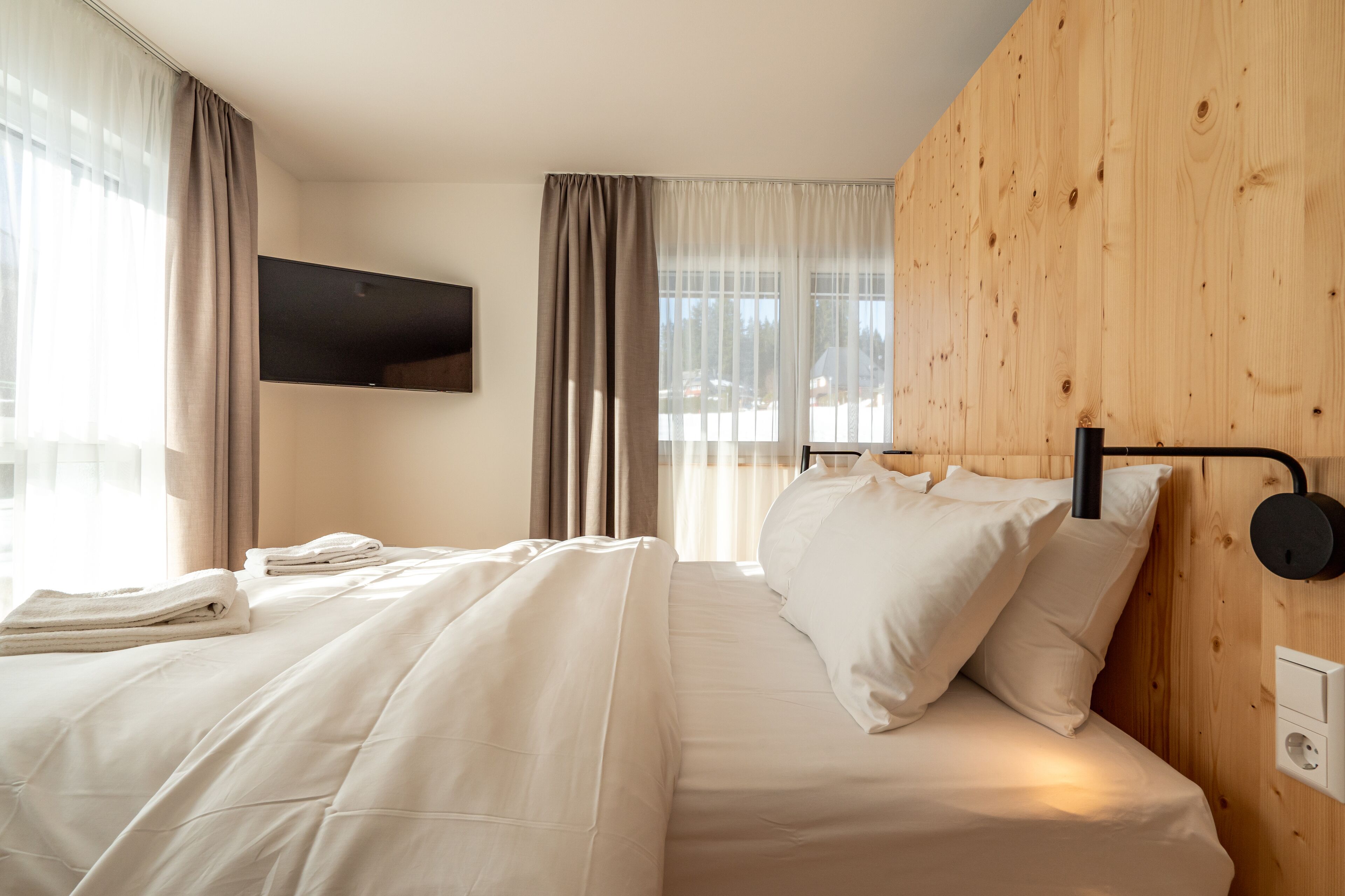 A hotel room with a bed, a flat-screen TV mounted on the wall, and a wooden panel wall.