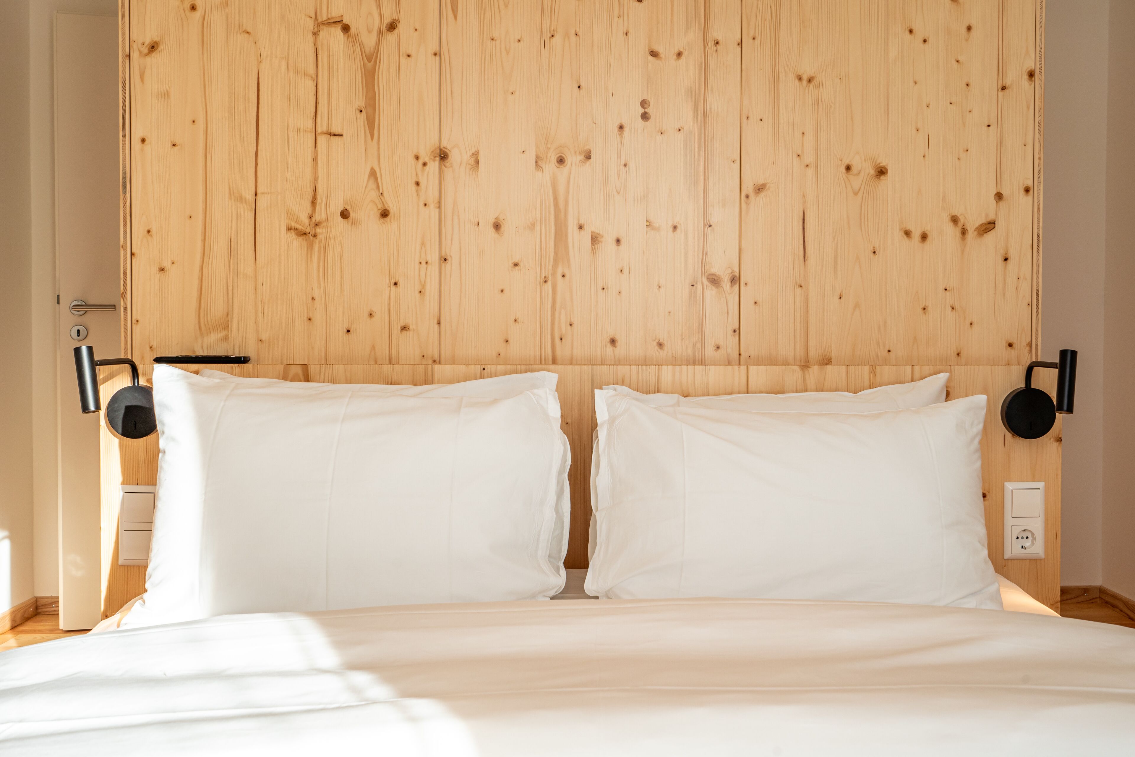 Een slaapkamer met een houten hoofdbord, twee witte kussens en een nachtkastje met een lamp.