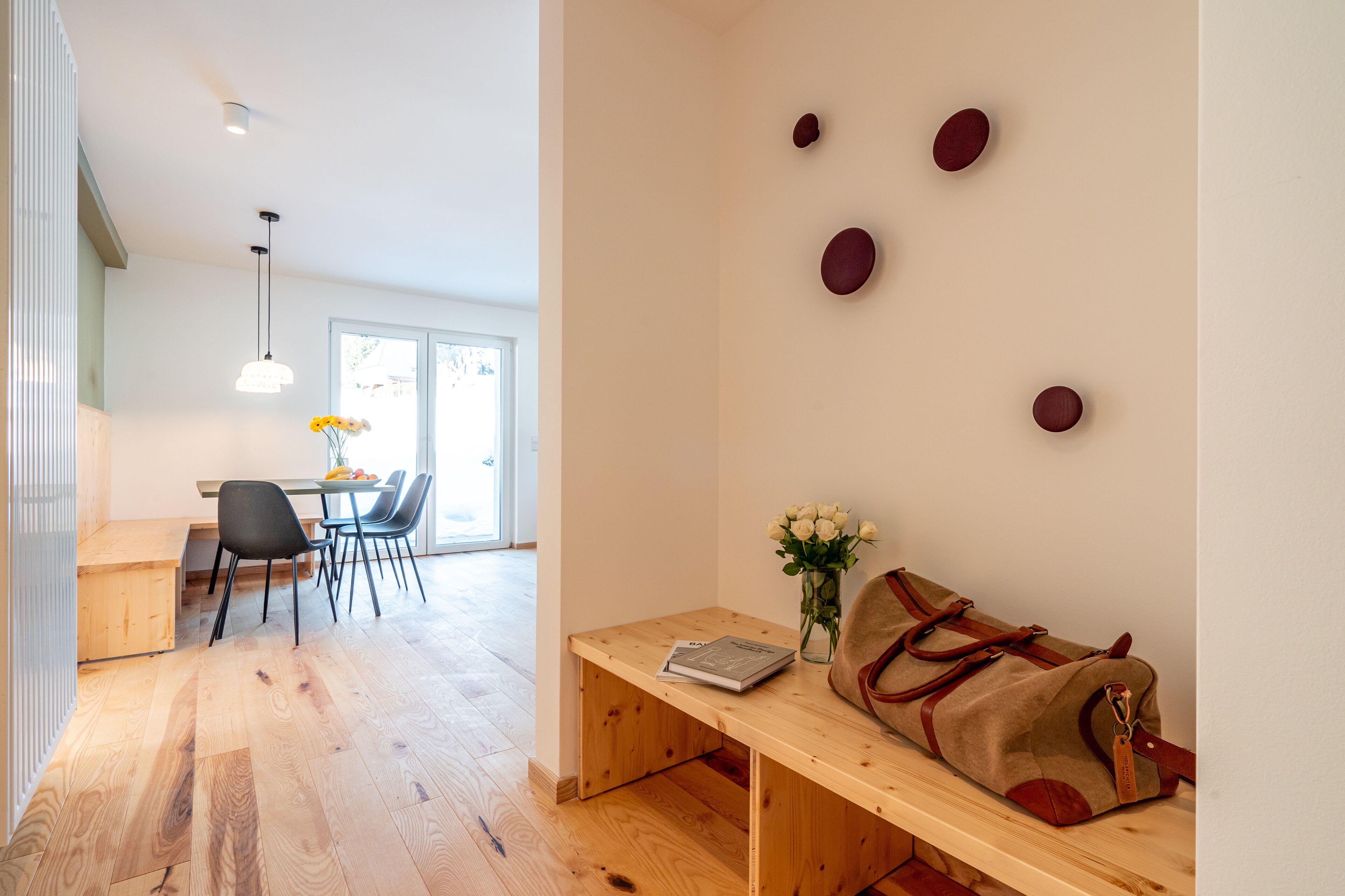 Una habitación moderna con un banco de madera, una mesa, un florero con flores y un bolso.