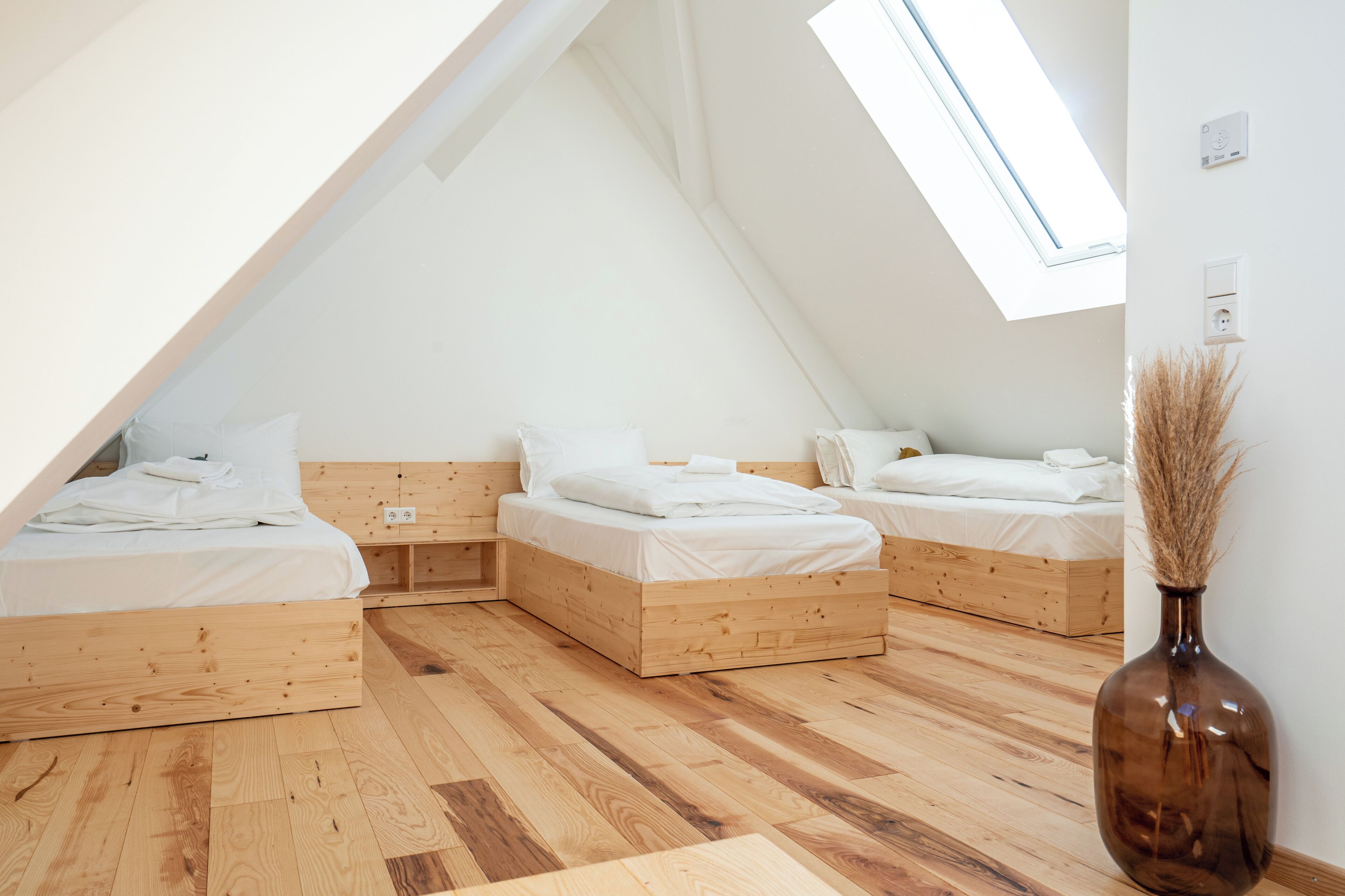 Een zijaal slaapkamer met drie houten bedden, een dakraam en een vaas met gedroogde planten.