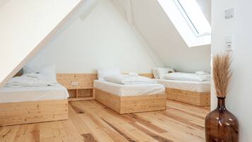 Een zijaal slaapkamer met drie houten bedden, een dakraam en een vaas met gedroogde planten.