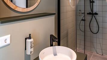 A modern bathroom with a round mirror, a white sink, and a glass-enclosed shower area.