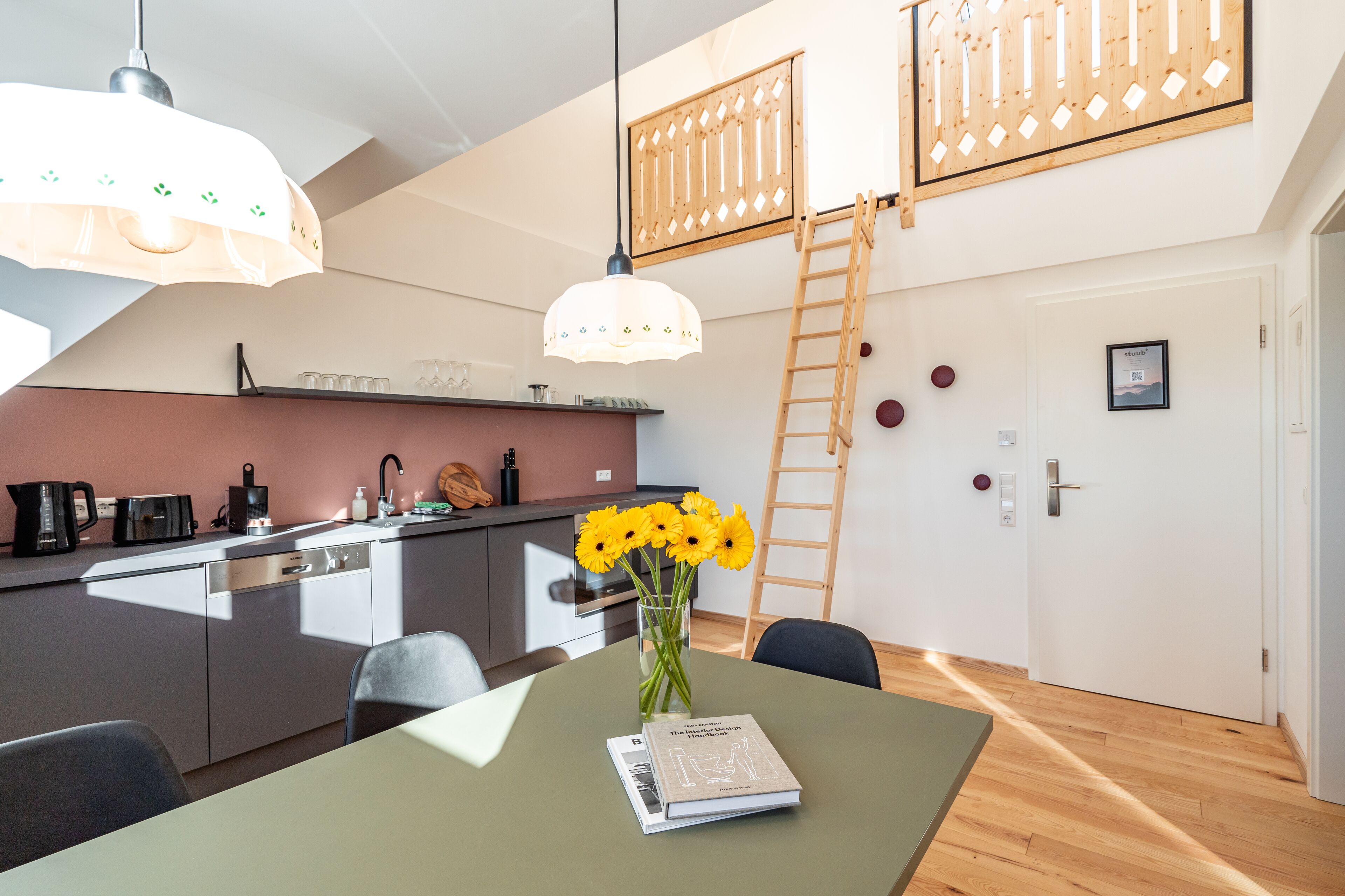 A modern kitchen with a dining area, a wooden ladder, and a vase of sunflowers on the table.