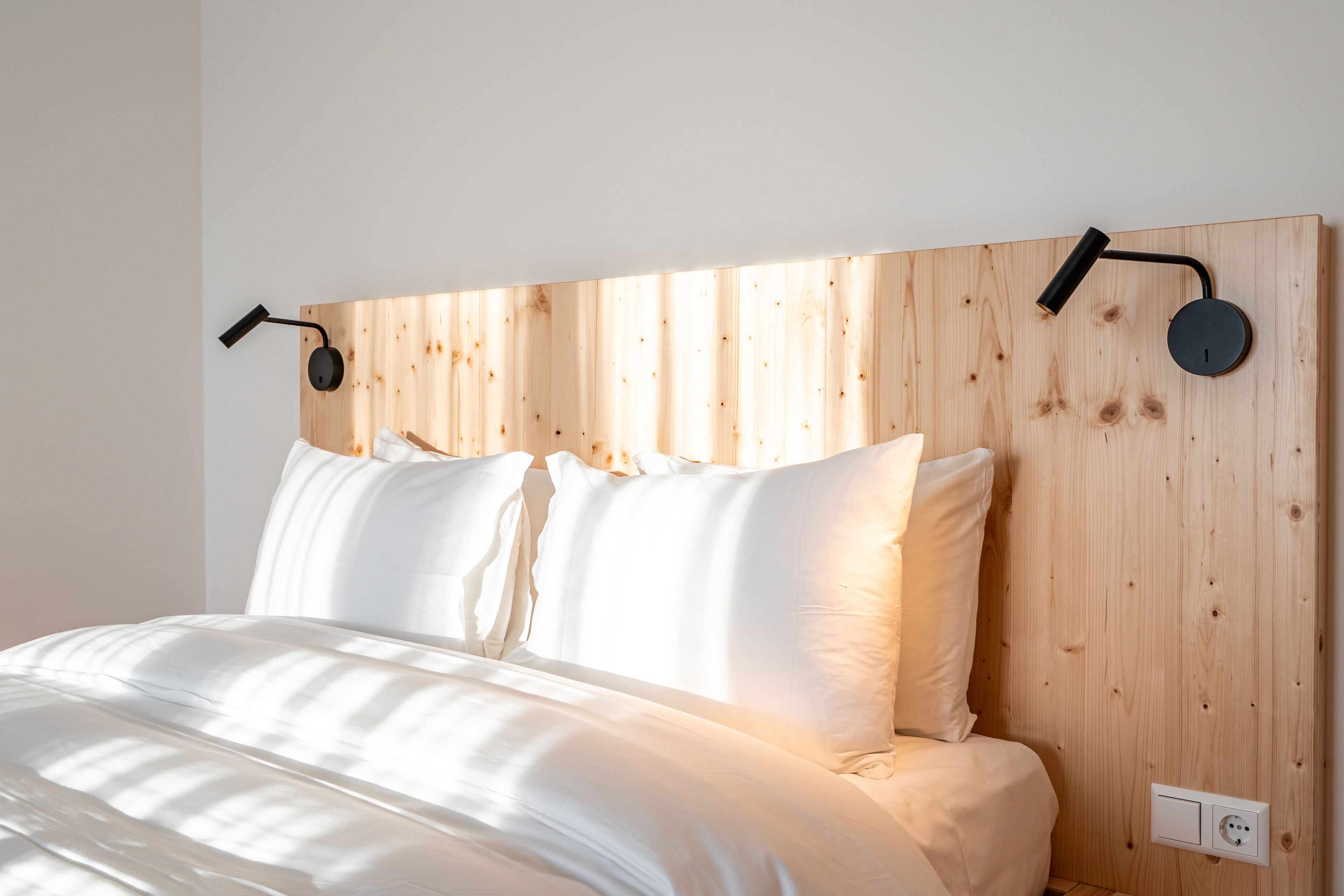 A bed with white bedding, a wooden headboard, and two wall-mounted reading lamps.