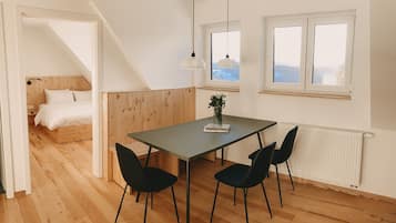 Ein modernes Zimmer mit Holzboden, einem Esstisch mit Stühlen, einem Bett mit Holzvorzelt und einem Fenster mit Blick.