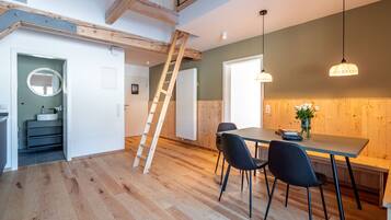 A modern kitchen with wooden flooring, a dining table with chairs, pendant lights, and a wooden ceiling.