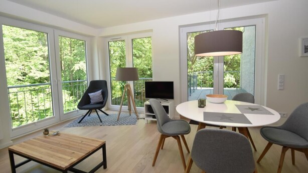 A modern living room with large windows, a round dining table, and a flat-screen TV. - fewo1846 - Smucke Utkiek (Glücksburg)