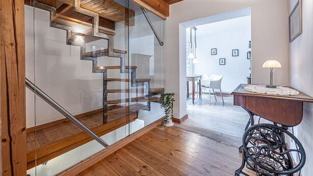 Un intérieur moderne avec un escalier en bois, un coin repas comprenant une table et des chaises, et un bureau avec une lampe.