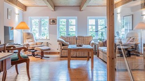 Un salon spacieux doté de parquet et d’un plafond haut, comprenant un ensemble de canapés, une table basse et un téléviseur.