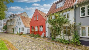 Une rue pavée bordée de bâtiments européens traditionnels, présentant un mélange de styles architecturaux et agrémentée d’un charmant banc.