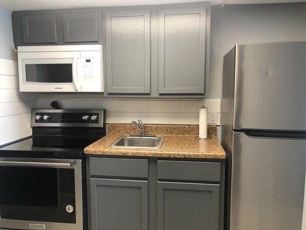 A kitchen with grey cabinets, a stainless steel refrigerator, a microwave, a stove, and a sink.