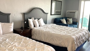 Habitación de hotel con dos camas, una mesita de noche, un espejo y una ventana con un equipo de aire acondicionado.