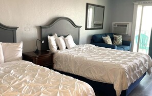 Ein Hotelzimmer mit zwei Betten, einem Nachttisch, einem Schminktisch und einem Fenster mit Klimaanlage.
