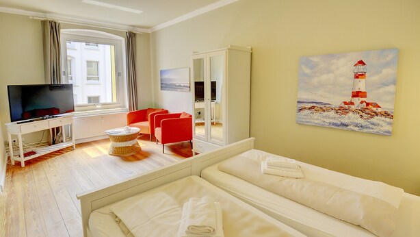 A hotel room with a bed, a TV, a desk, and a painting of a lighthouse. - fewo1846 - Am Südermarkt / centrally located 2-room apartment. on the 2nd floor (Flensburg)