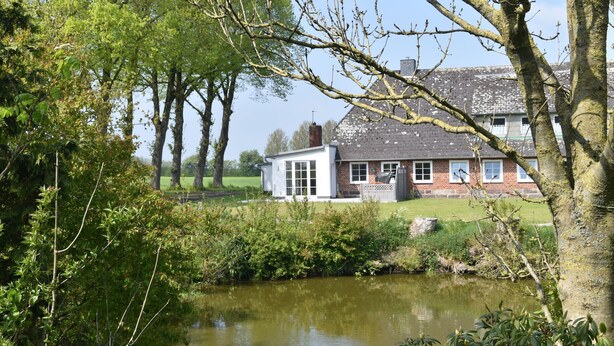 Een huis met een bakstenen gevel en witte ramen, omringd door bomen en een vijver.