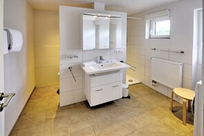 Une salle de bain moderne avec un lavabo blanc, un miroir et un meuble-lavabo. Une fenêtre laisse entrer la lumière naturelle et un radiateur assure le chauffage.