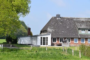 Une maison à deux étages, dotée d’un toit en pente, d’une partie en briques et d’une partie blanche avec de grandes fenêtres.