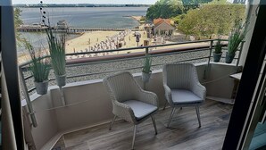 A balcony with wicker chairs and potted plants, overlooking a beach and a pier. - fewo1846 - Kajüte Fördeblick (App. 112) / family-friendly studio apartment (Glücksburg)