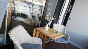 A balcony with wicker chairs and a wooden table, a vase with flowers, and a view of the outside. - fewo1846 - Kajüte Fördeblick (App. 112) / family-friendly studio apartment (Glücksburg)
