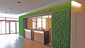 A reception area with a green textured wall, a reception desk, and a glass door leading to a hallway. - fewo1846 - Kajüte Fördeblick (App. 112) / family-friendly studio apartment (Glücksburg)