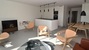 Ein modernes Wohnzimmer mit Fernseher, Sitzgelegenheiten und einer Küchenzeile.
