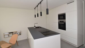 Eine moderne Küche mit einer zentralen Kochinsel, integrierten Geräten und Pendelleuchten.