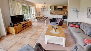 A living room with a TV, sofa, and coffee table. There is a kitchen in the background with cabinets and a microwave.