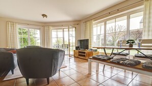 A spacious living room with a large window, a television, and a bench with cushions.