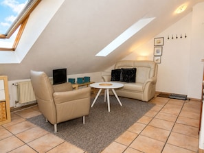 Une chambre confortable aménagée en mezzanine, avec un plafond en pente, un téléviseur à écran plat, un canapé, une table basse et un petit tapis.