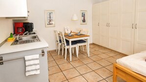 A compact kitchen with a sink, a coffee machine, and a dining area with chairs and a table. There is a bed with a white mattress and a wooden headboard. - fewo1846 - Little Mermaid (App. 666) / studio apartment in the attic (Harrislee)