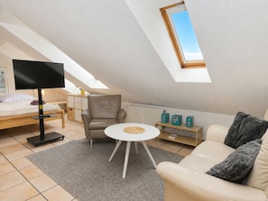 Une chambre de style loft moderne avec un plafond en pente, un lit, un coin salon avec un canapé et un fauteuil, une petite table ronde et un téléviseur.