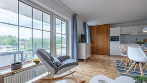 Eine moderne Wohnung mit großem Fenster, einer Küche, einem Essbereich und einem Wohnzimmer mit Schaukelstuhl.