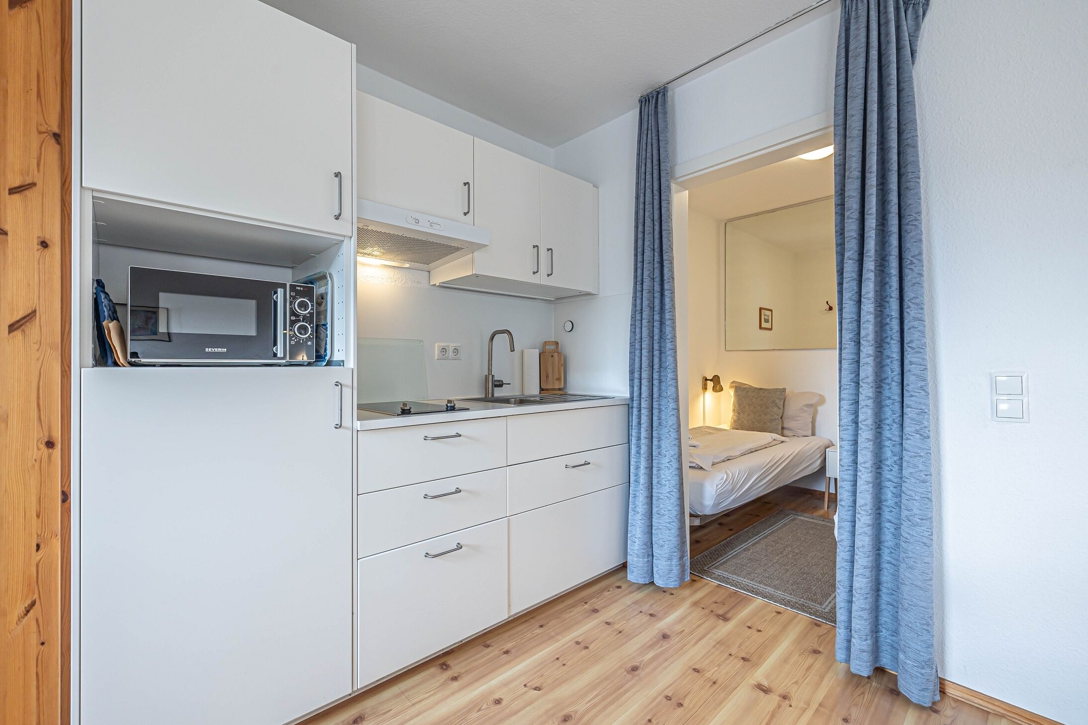 Een kleine keuken met witte kastjes, een magnetron en een spoelbak.