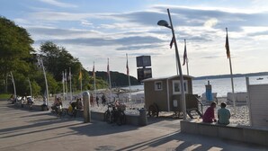 Rantakadulla on pieni kioski, pyöriä ja ihmisiä kävelemässä.