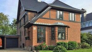 A two-story brick house with a sloped roof, a garage, and a well-maintained garden with flowers and shrubs.