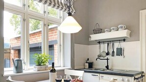 A kitchen with a window, a table with a striped tablecloth, and various kitchen utensils hanging on the wall.