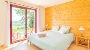 A bedroom with a bed, pillows, a nightstand with a lamp, and a sliding glass door leading to an outdoor seating area.