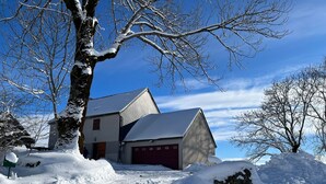 A snow-covered house with a garage, a tree in the foreground, and a clear blue sky.