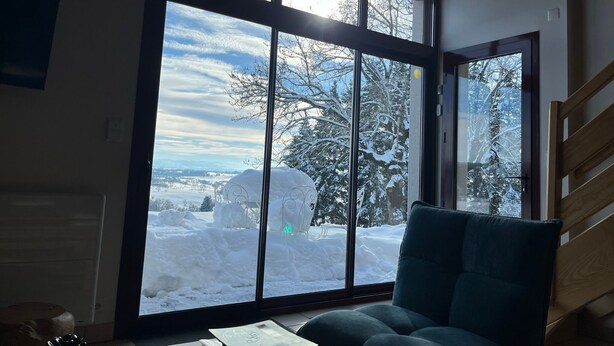 A room with a large window overlooking a snowy landscape, a green armchair, and a wooden staircase.