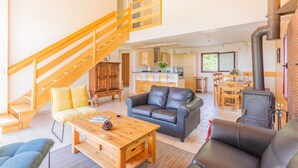A spacious living area with a wooden staircase, a black leather sofa, a wooden coffee table, and a kitchen in the background.