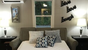 A bedroom with a bed, two nightstands, a window, and a wall decoration saying "Love Love Laugh".