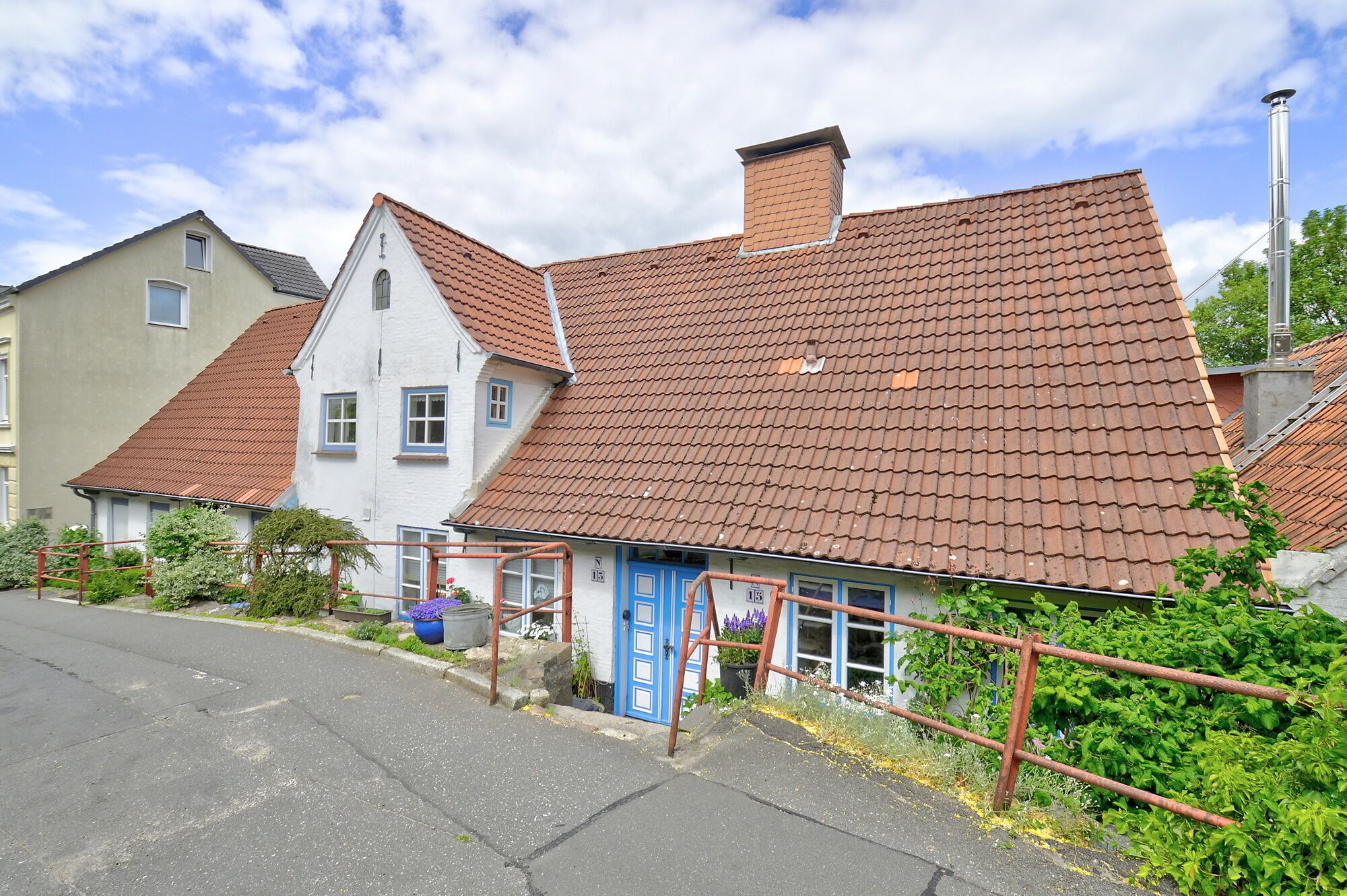 Une rangée de maisons traditionnelles avec des toits couverts de tuiles rouges, une porte bleue et un petit jardin.