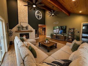 A living room with a stone fireplace, a large sofa set, a television, and a ceiling fan.