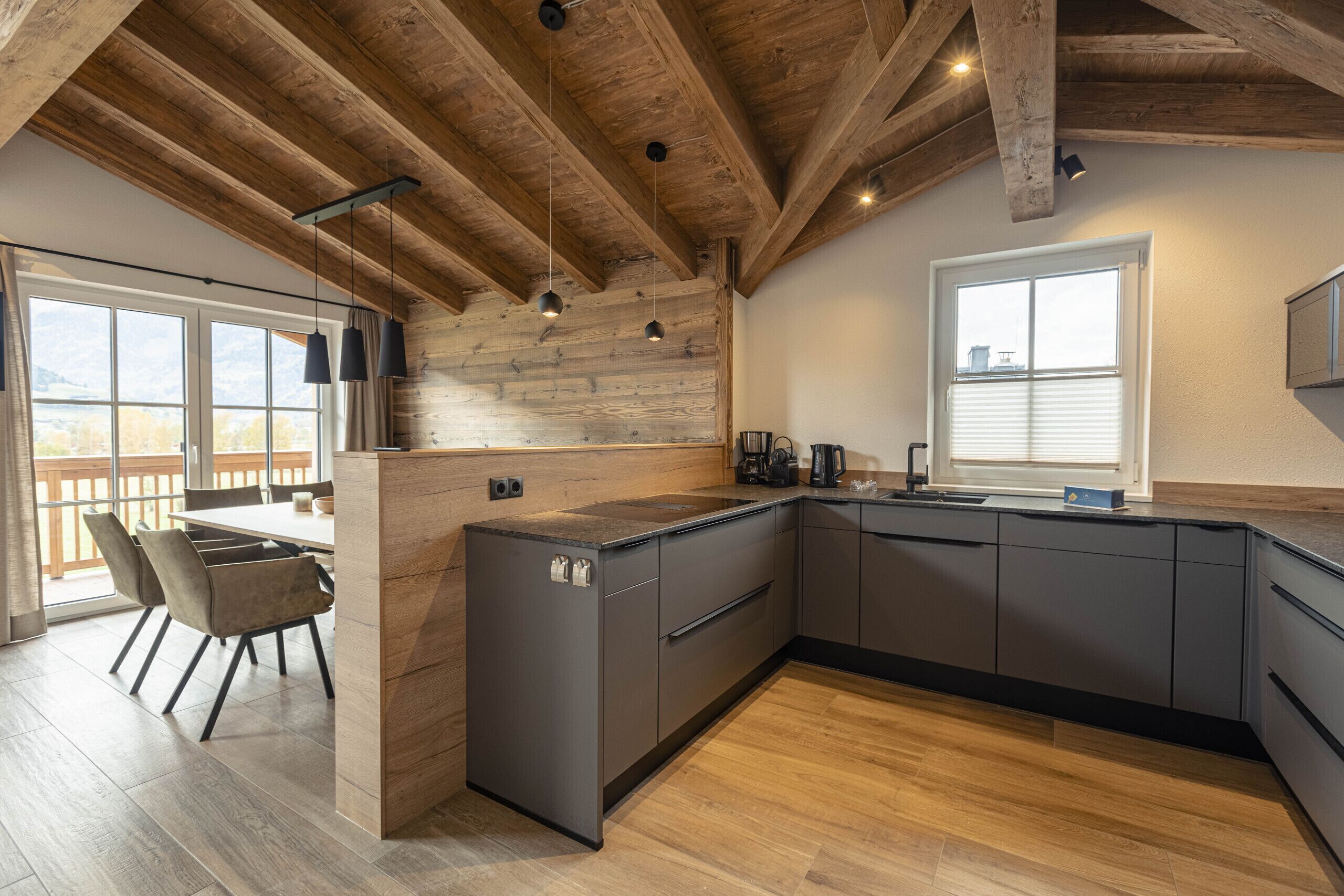 A modern kitchen with wooden beams, a large island, and a view of the outdoors.