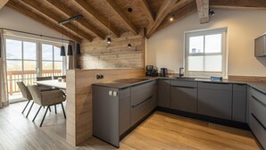 A modern kitchen with wooden beams, a large island, and a view of the outdoors. - Superior chalet # 2A with sauna (Uttendorf)