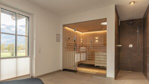 A modern bathroom with a glass shower enclosure, wooden cabinets, and a view of mountains through a large window. - Superior chalet # 2A with sauna (Uttendorf)