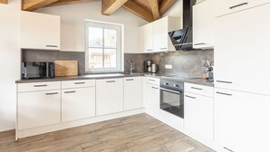 Une cuisine moderne avec des armoires blanches, un four encastré et une fenêtre donnant sur l’extérieur.